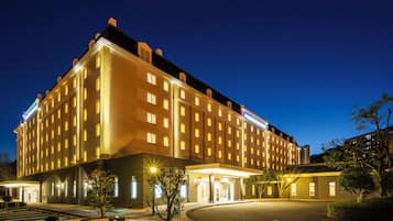 A large, multi-story hotel with a well-lit facade and a parking area in front.