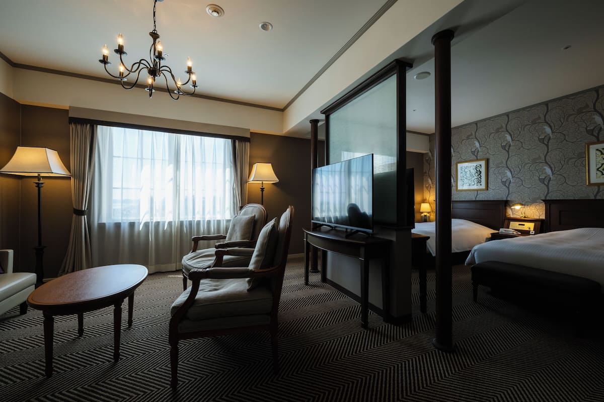 Ein Hotelzimmer mit einem großen Bett, einem Fernseher, einem Schreibtisch mit Stuhl, einer Couch und einem Chandelier.