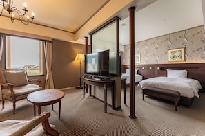 A hotel room with a bed, a television, a chair, a small table, and a view of the outside.