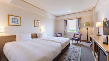 A hotel room with two beds, a desk, a chair, a window with curtains, and a lamp.