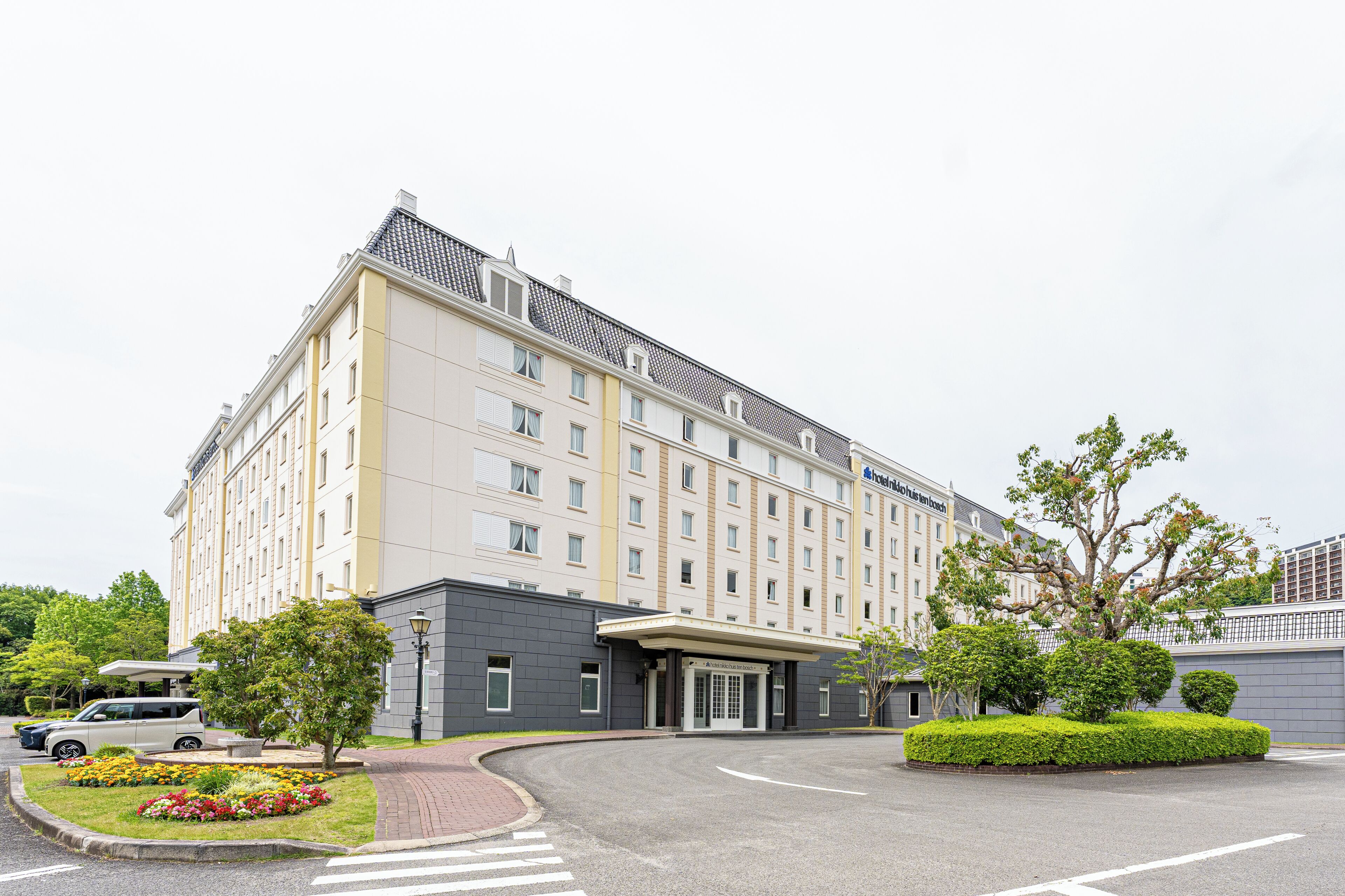 A multi-story hotel with a modern facade, a gated entrance, and a landscaped driveway.