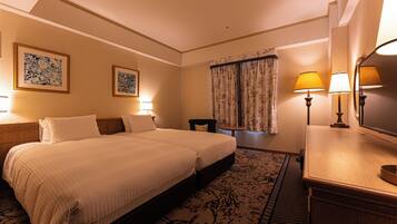 A hotel room with a double bed, two bedside tables with lamps, a small chair, a desk with a lamp, and a large mirror.