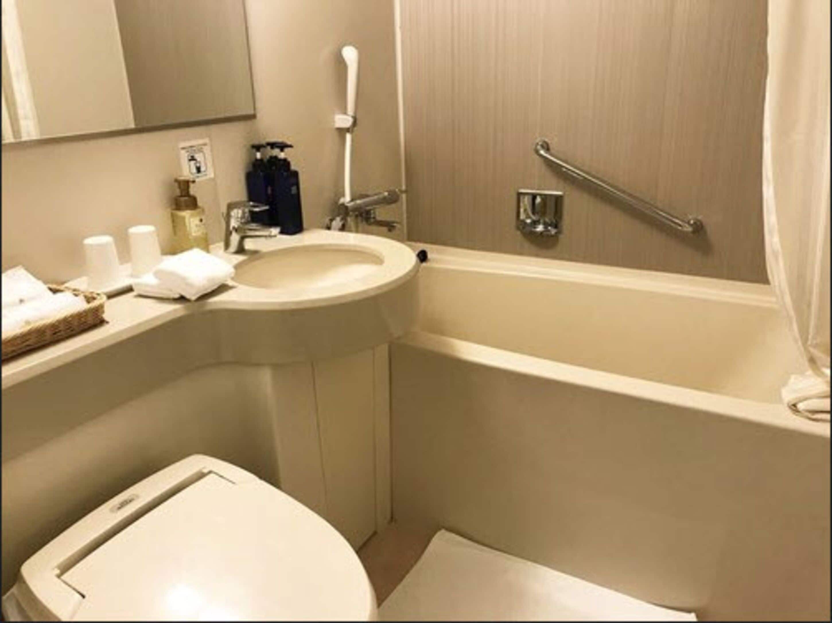 A bathroom with a sink, toilet, and bathtub. There is a handrail in the bathtub and a towel rack above the sink.