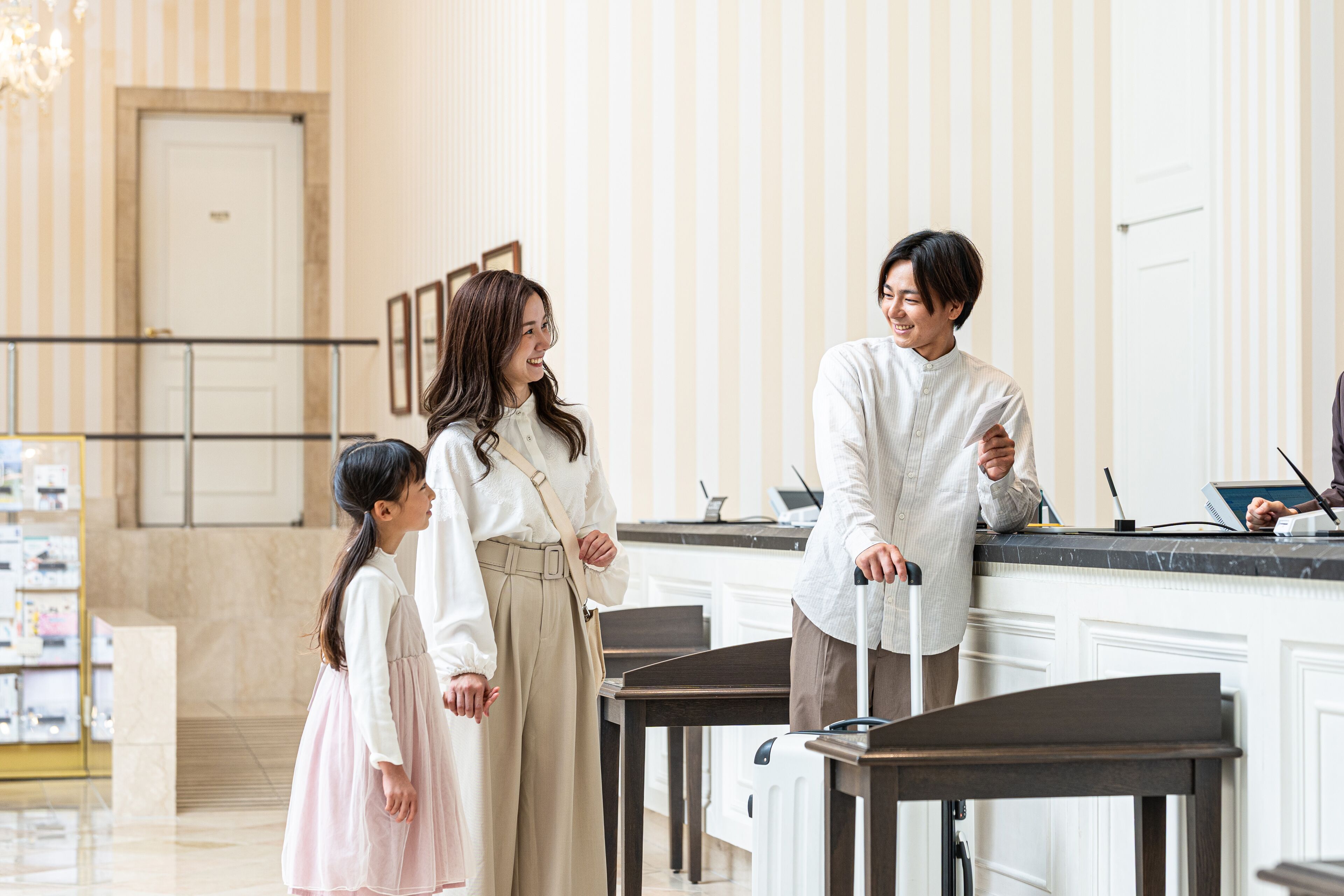 Eine Hotellobby mit einer Rezeption, einem Kind und einem Erwachsenen mit Koffer.
