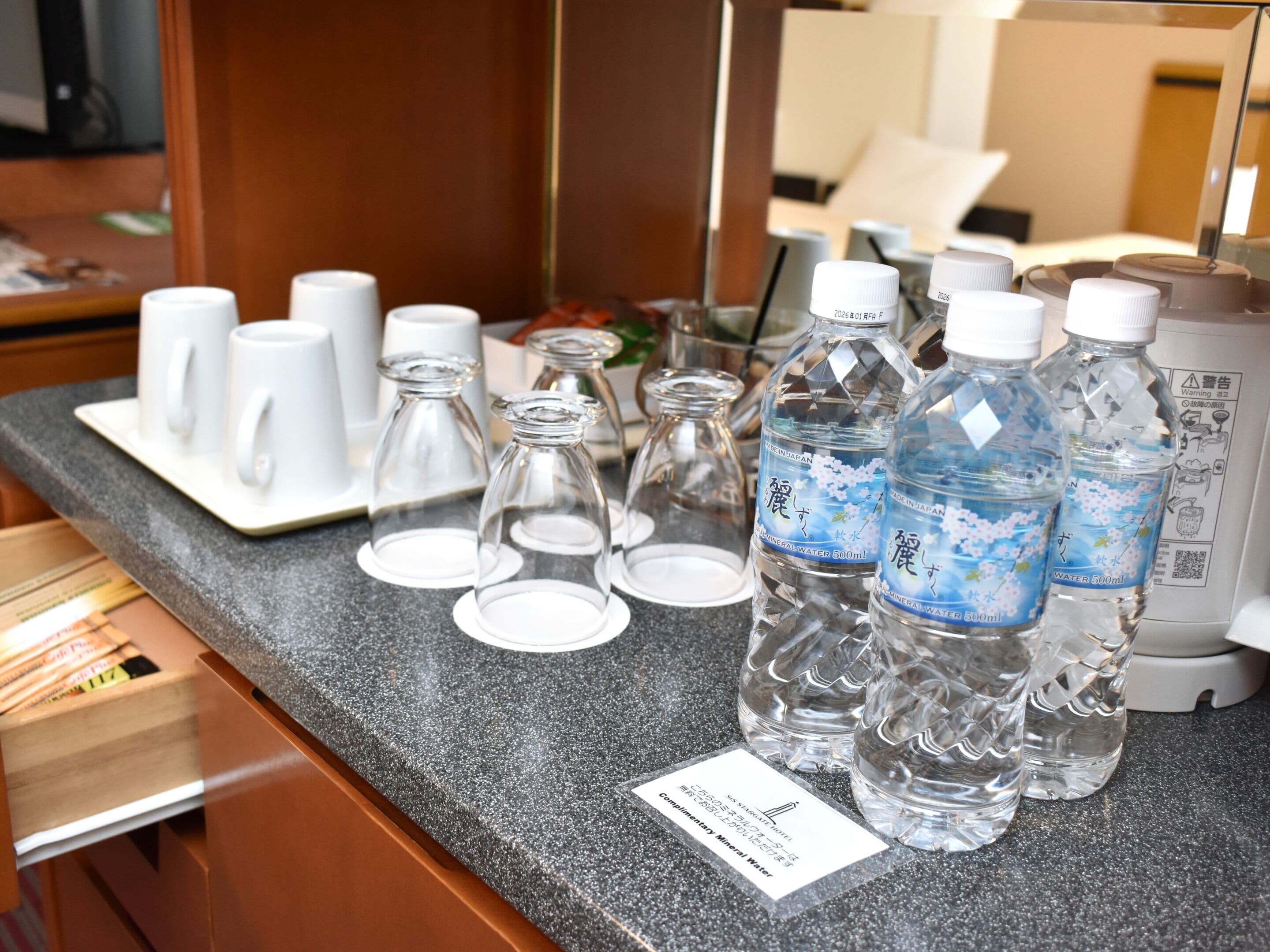 A hotel room counter with various amenities including a coffee maker, tea set, and mineral water bottles.