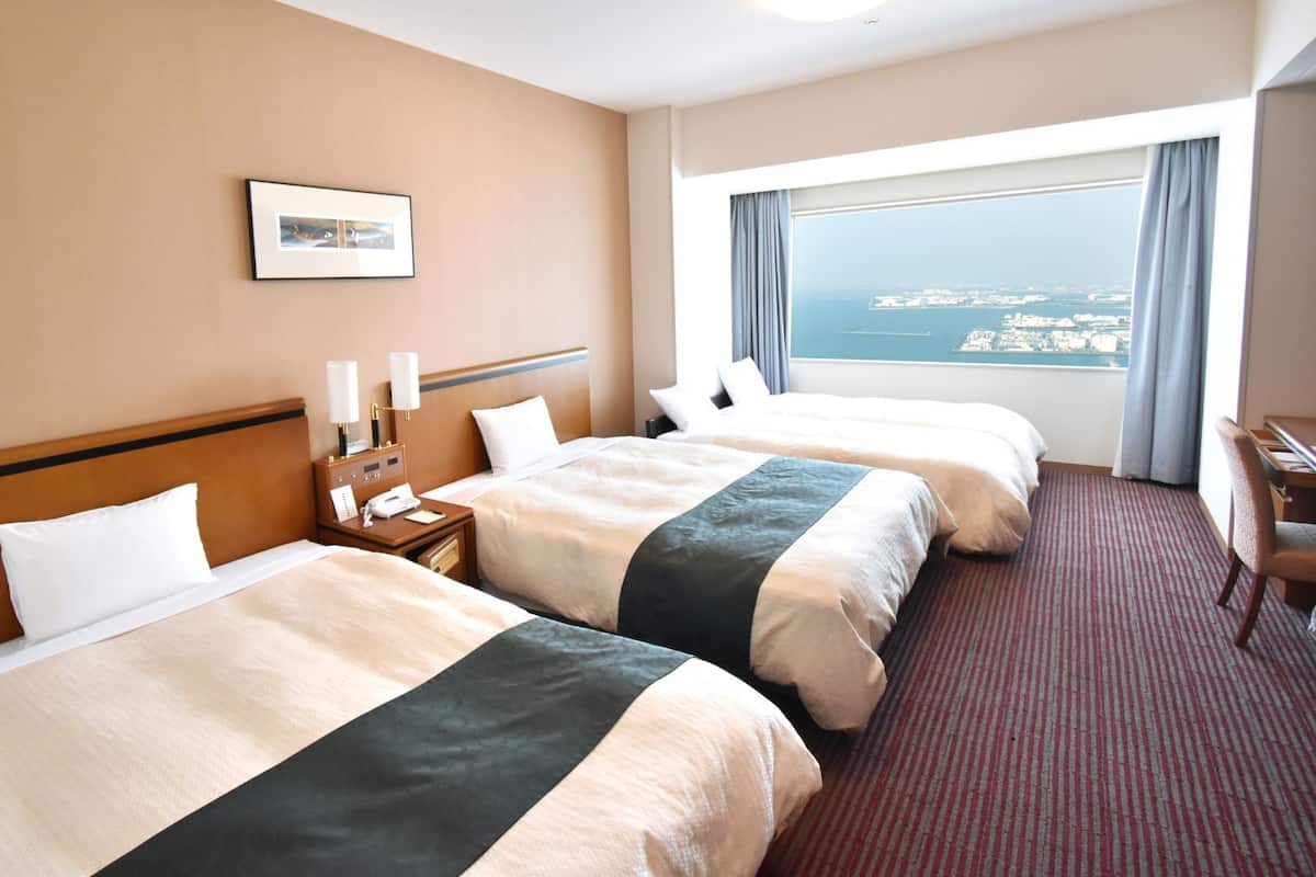 A hotel room with two beds, a desk, a chair, a nightstand with a lamp, a phone, and a window with a view.