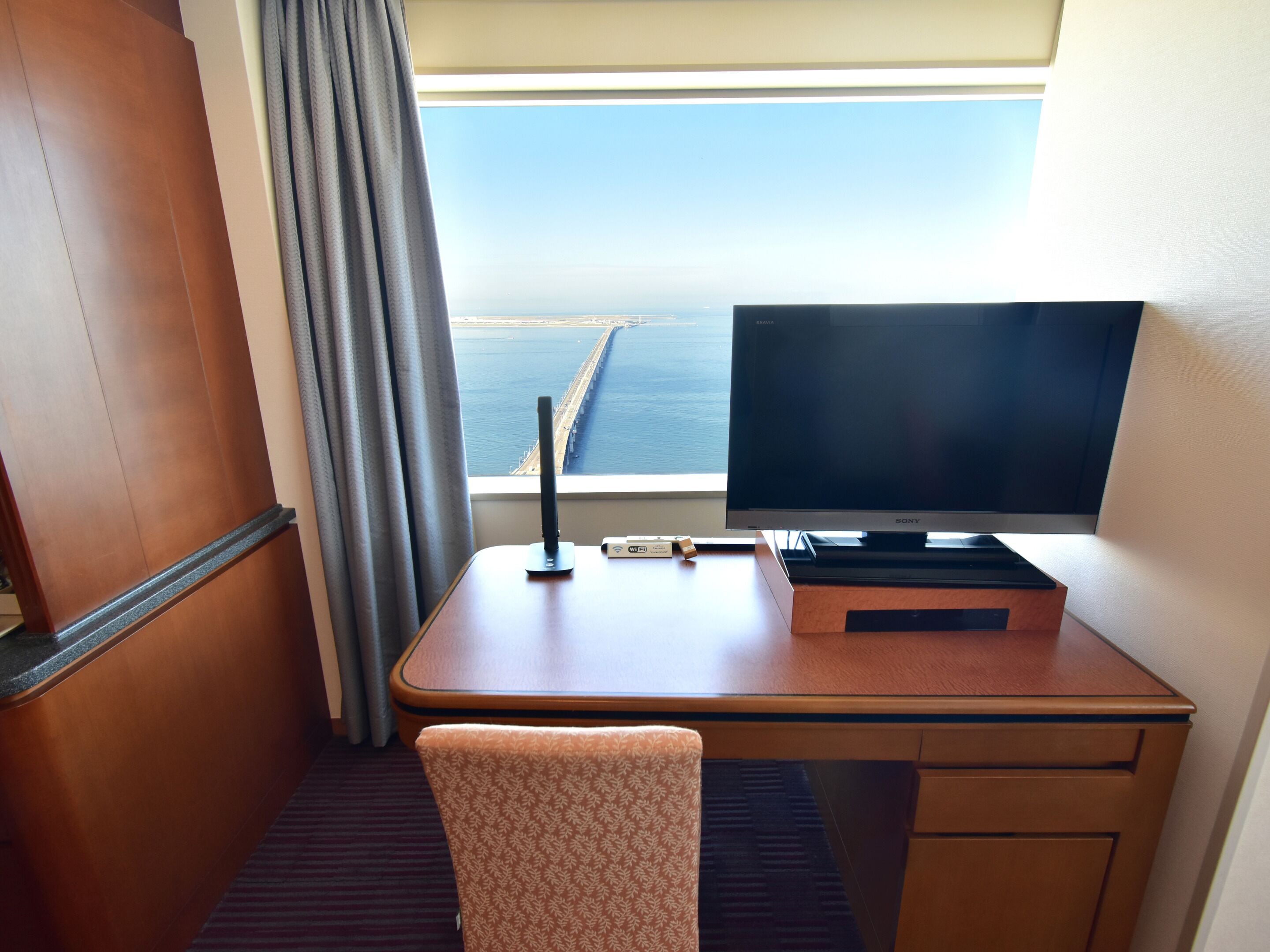 Une chambre d’hôtel avec un bureau en bois, une télévision et une vue sur un pont enjambant une étendue d’eau.