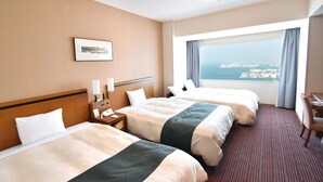 A hotel room with two beds, a desk, a chair, a nightstand, a lamp, a phone, a picture on the wall, and a large window with a view of the city. - Star Gate Hotel Kansai Airport (Izumisano)