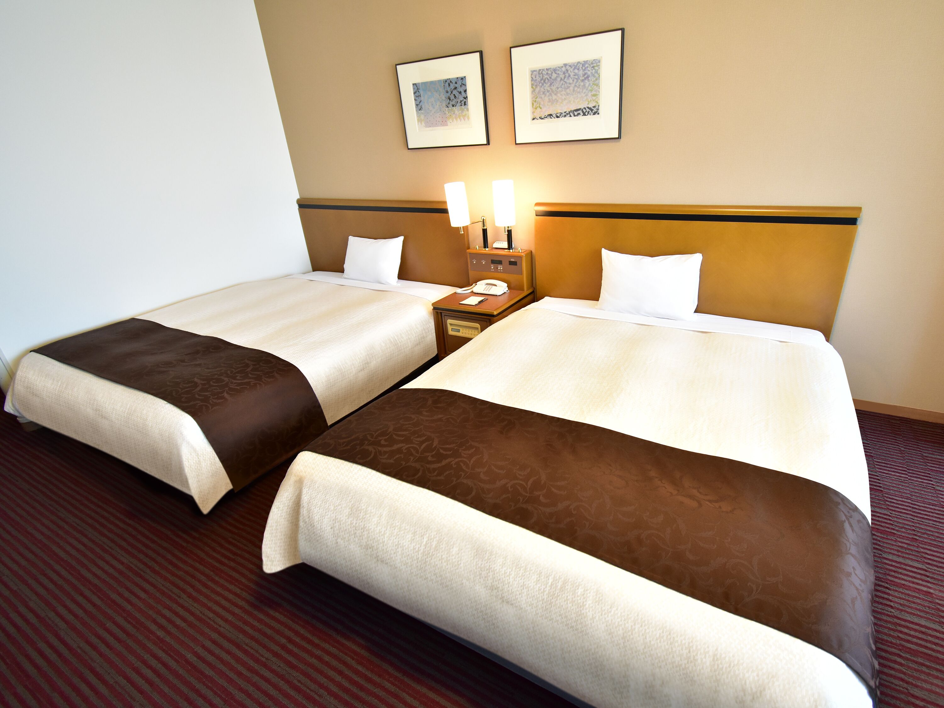 A hotel room with two beds, a nightstand with a lamp, and two framed pictures on the wall.