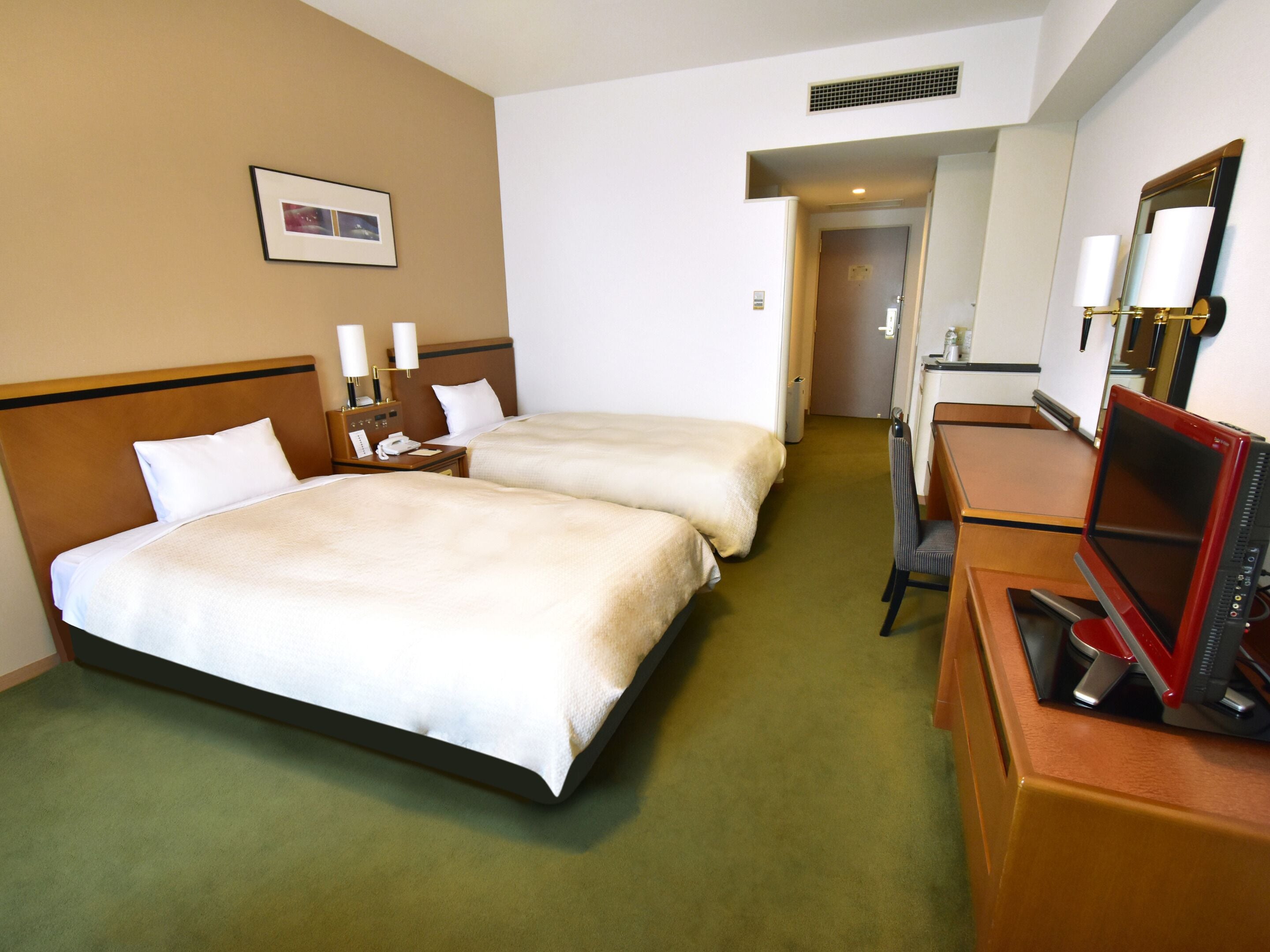 Una habitación de hotel con dos camas, un escritorio con una computadora, una silla y un espejo.