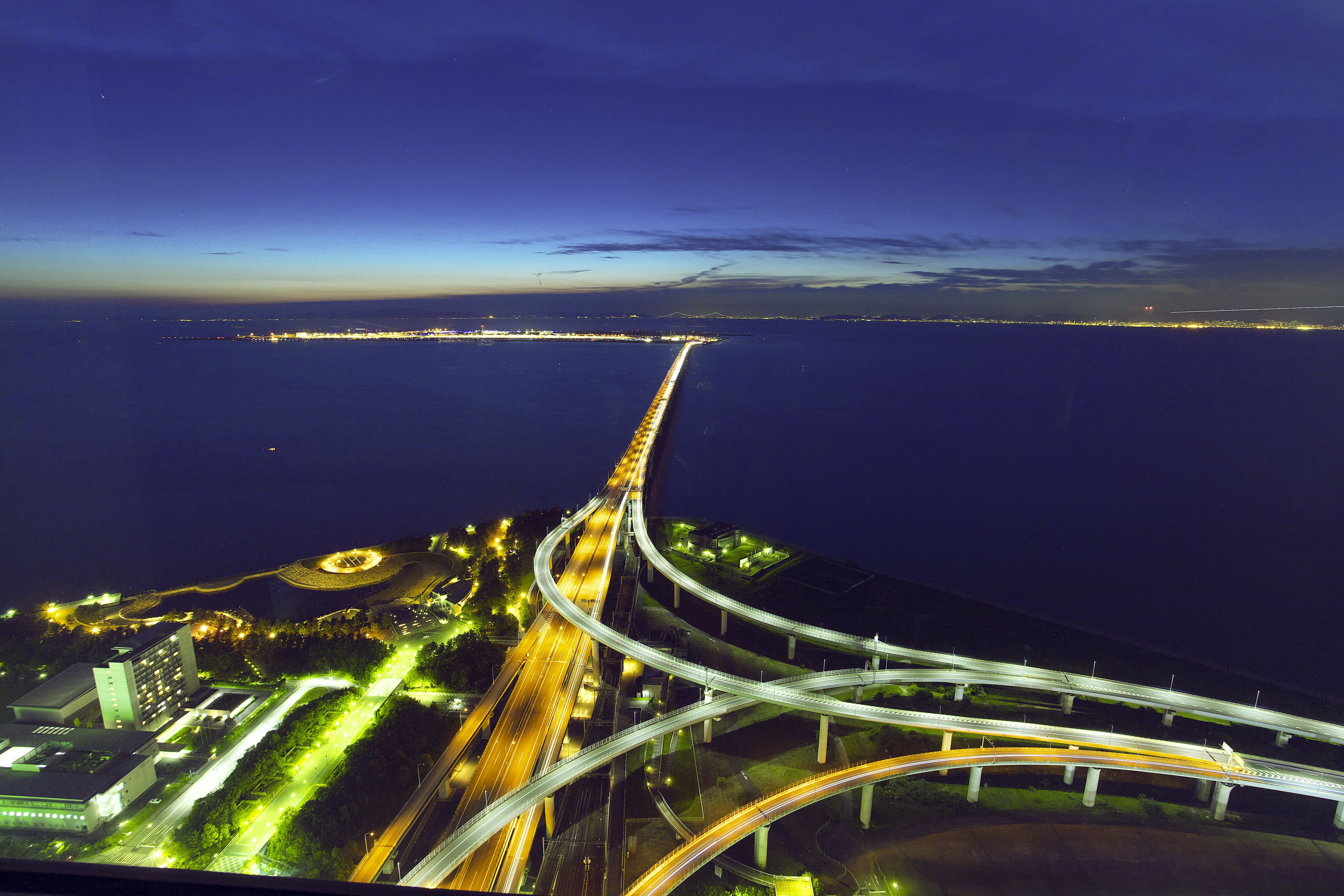 A multi-level highway interchange with overhead bridges and a long bridge extending into the water.