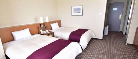A hotel room with two beds, a nightstand with a phone and lamps, a framed picture on the wall, and a carpeted floor.