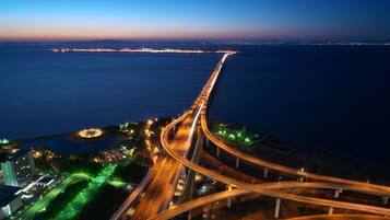 Vista aérea de un complejo intercambio de autopistas con puentes elevados y un paisaje urbano costero al fondo.