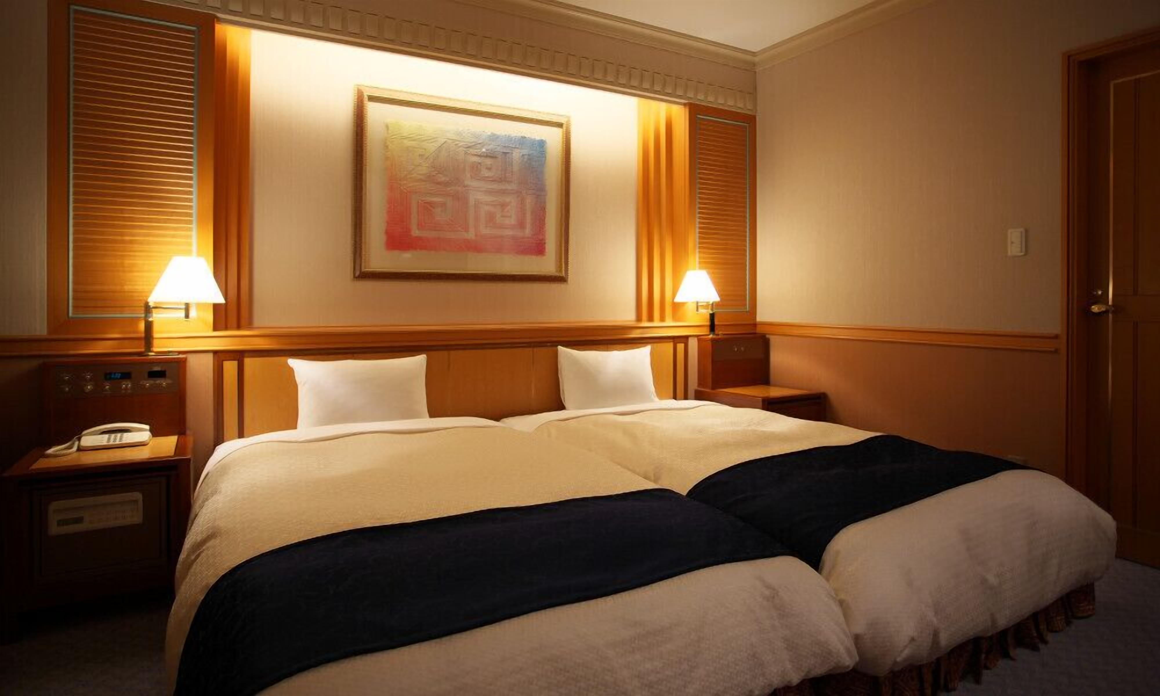 Une chambre d’hôtel avec un grand lit, deux tables de chevet, un téléphone et un tableau au mur.
