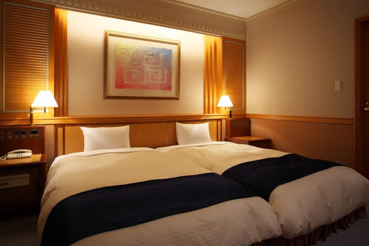 A hotel room with a large bed, two bedside tables, a phone, and a painting on the wall.