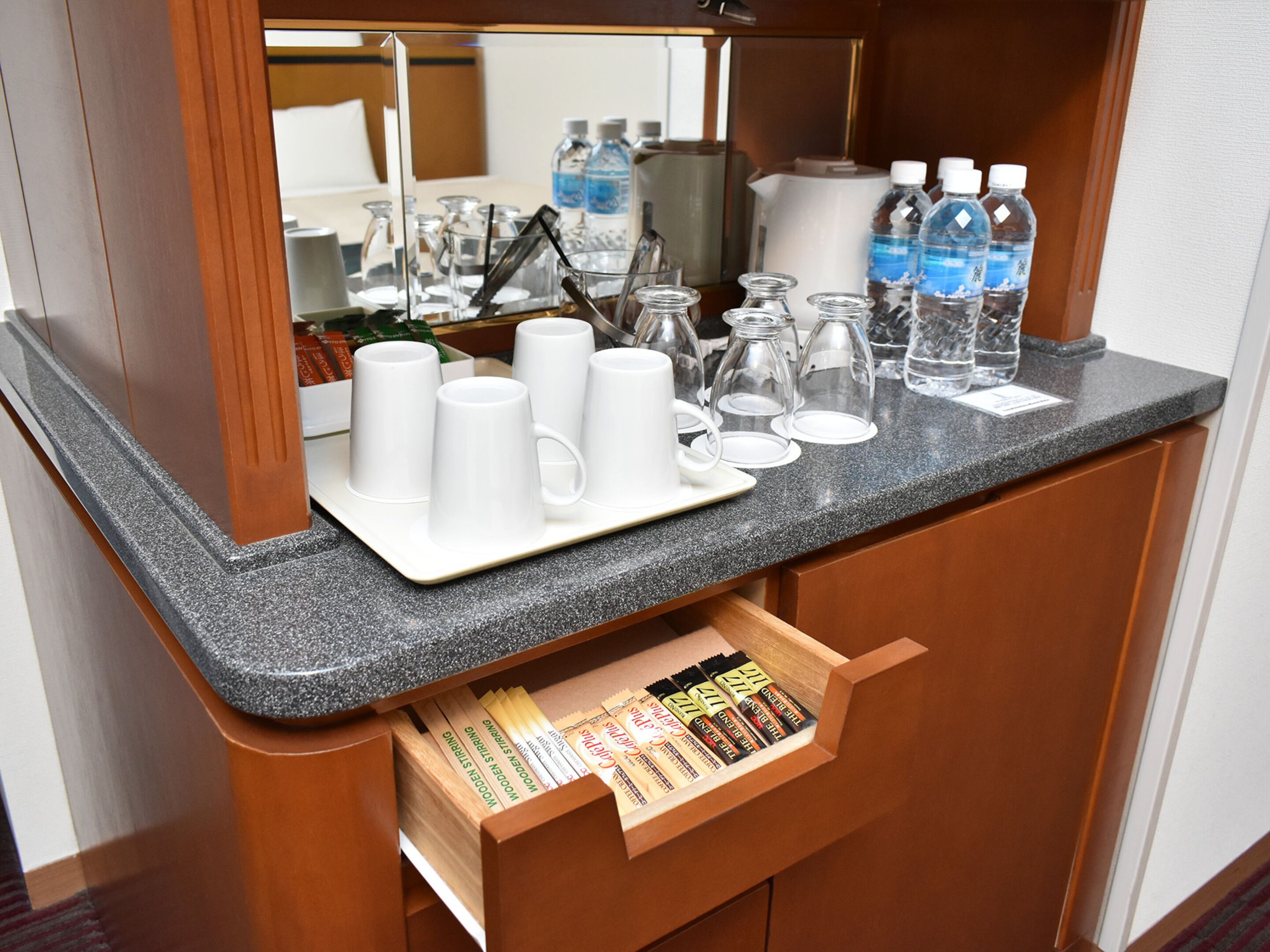 A hotel room's minibar with a tray of white cups, glasses, and bottles of water.