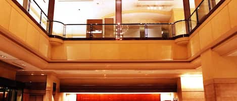 A hotel lobby with a reception desk, seating area, and a glass railing overlooking the lower level.