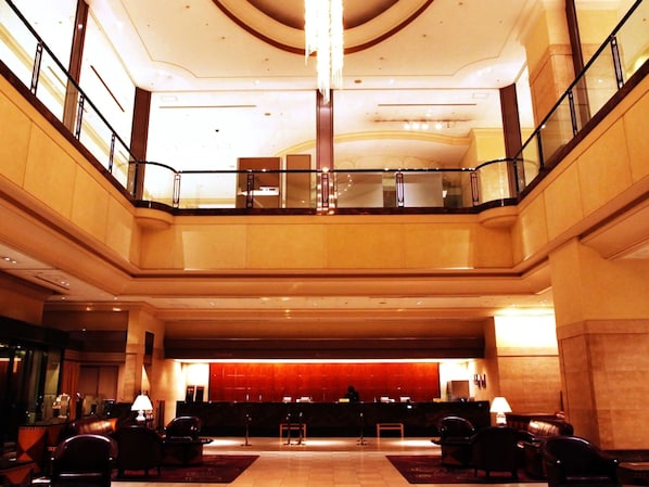 A hotel lobby with a reception desk, seating area, and a glass railing overlooking the lower level.