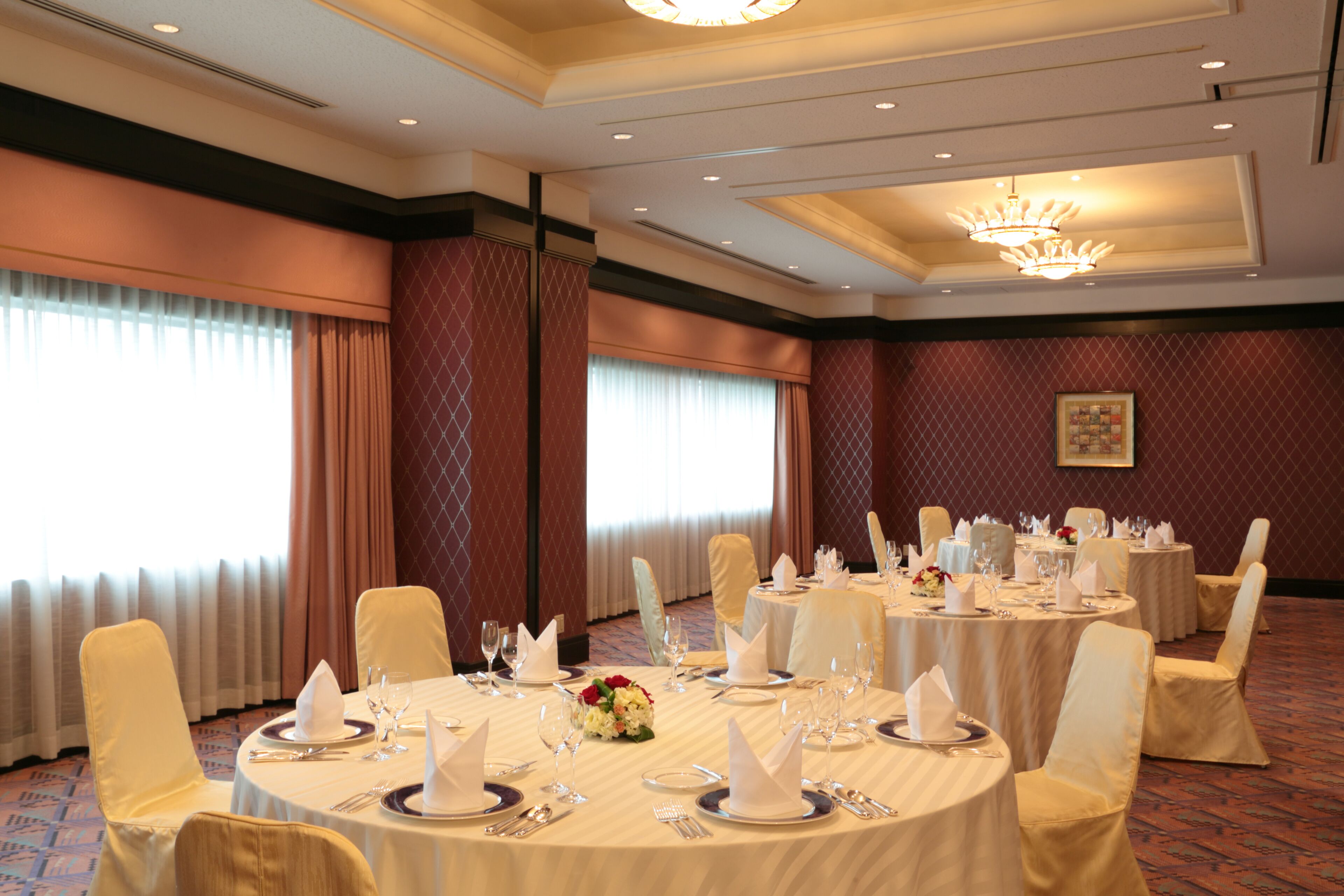 Un salón de banquetes con mesas redondas dispuestas para cenar, con manteles blancos, servilletas y cristalería.