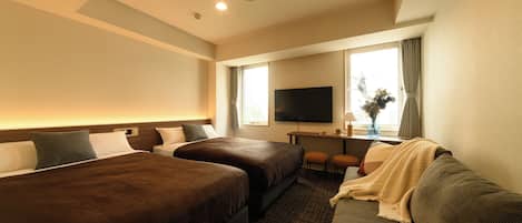A hotel room with two beds, a sofa, a TV, and a desk with a vase.