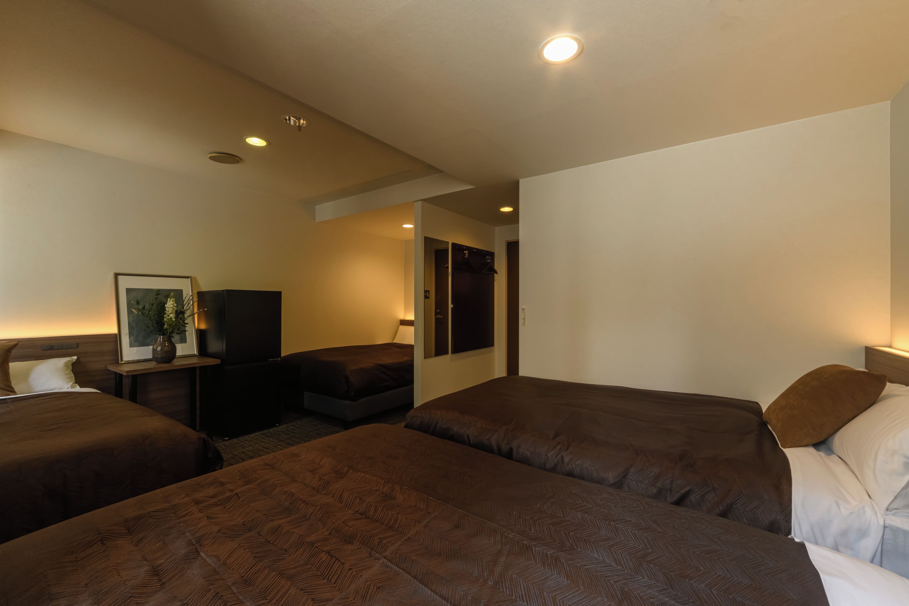 A hotel room with two beds, a desk, a chair, and a small table with a vase of flowers.