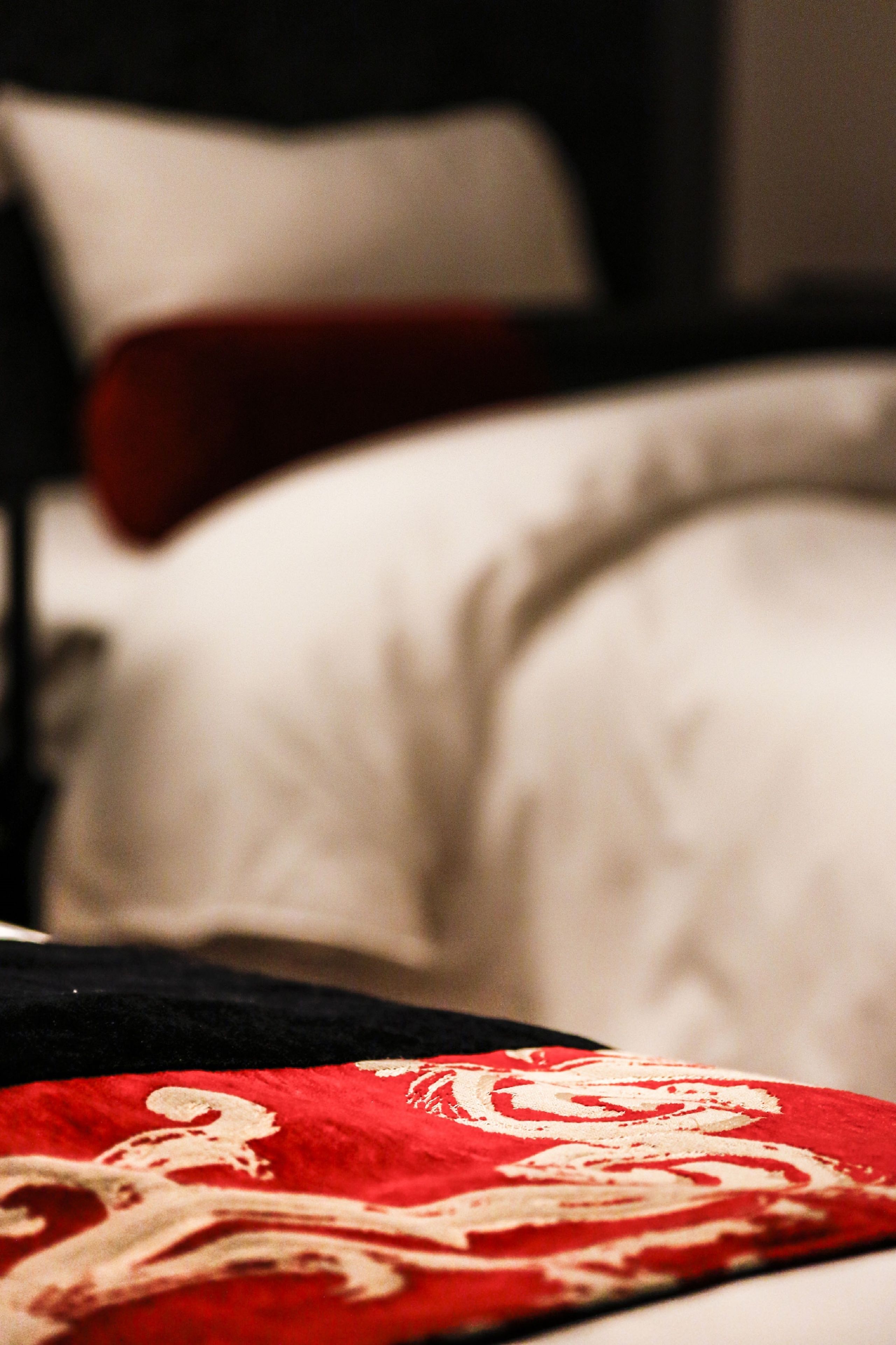 A bed with a red and white patterned blanket, a white pillow, and a red pillow.