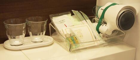 A bathroom counter with a hairdryer, two glasses, and a tray with toiletries.