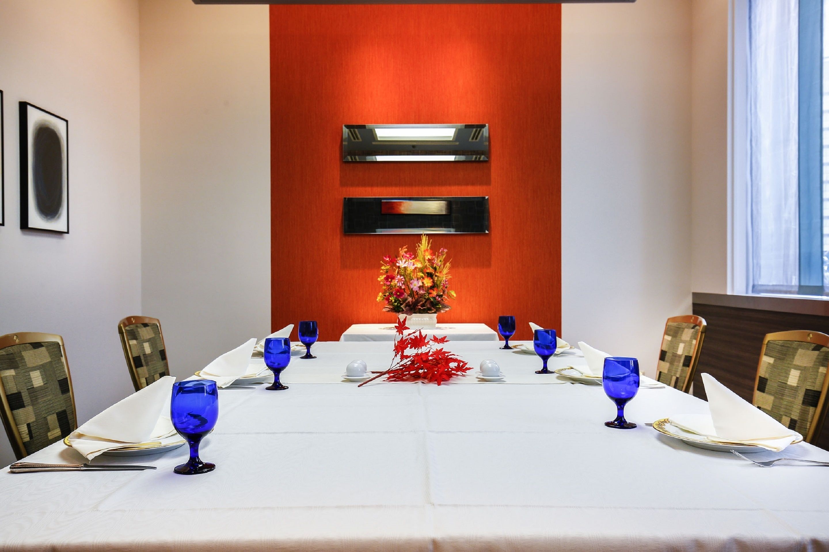 A dining table set for six with blue glassware, white napkins, and a vase of flowers.