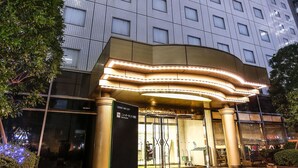 A modern hotel entrance with a tiled ground floor, a large building with multiple windows in the background, and illuminated signage. - New Otani Inn Tokyo (Tokyo)