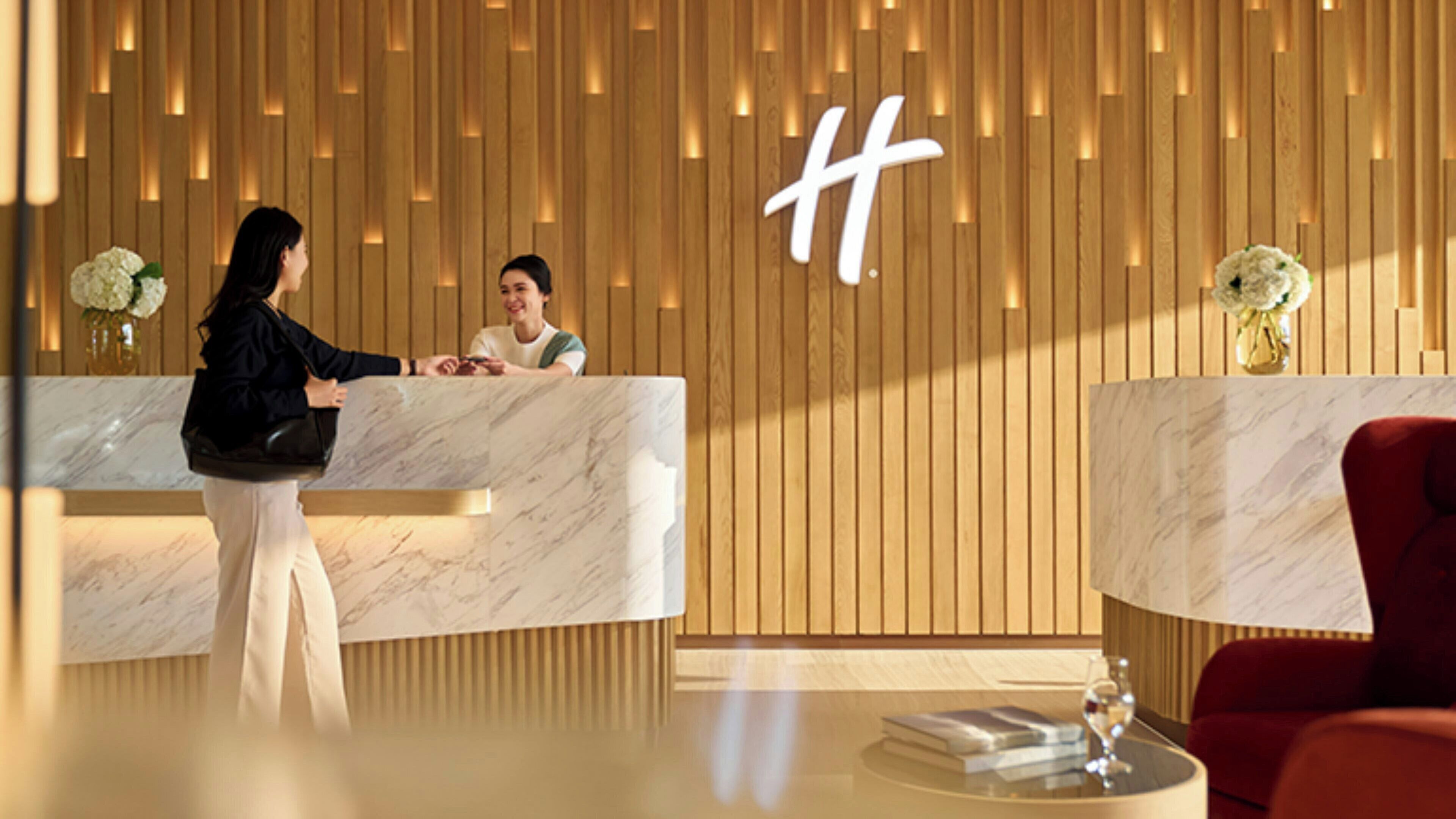 A hotel reception area with marble counters, wooden paneling, and a large 'H' logo on the wall.