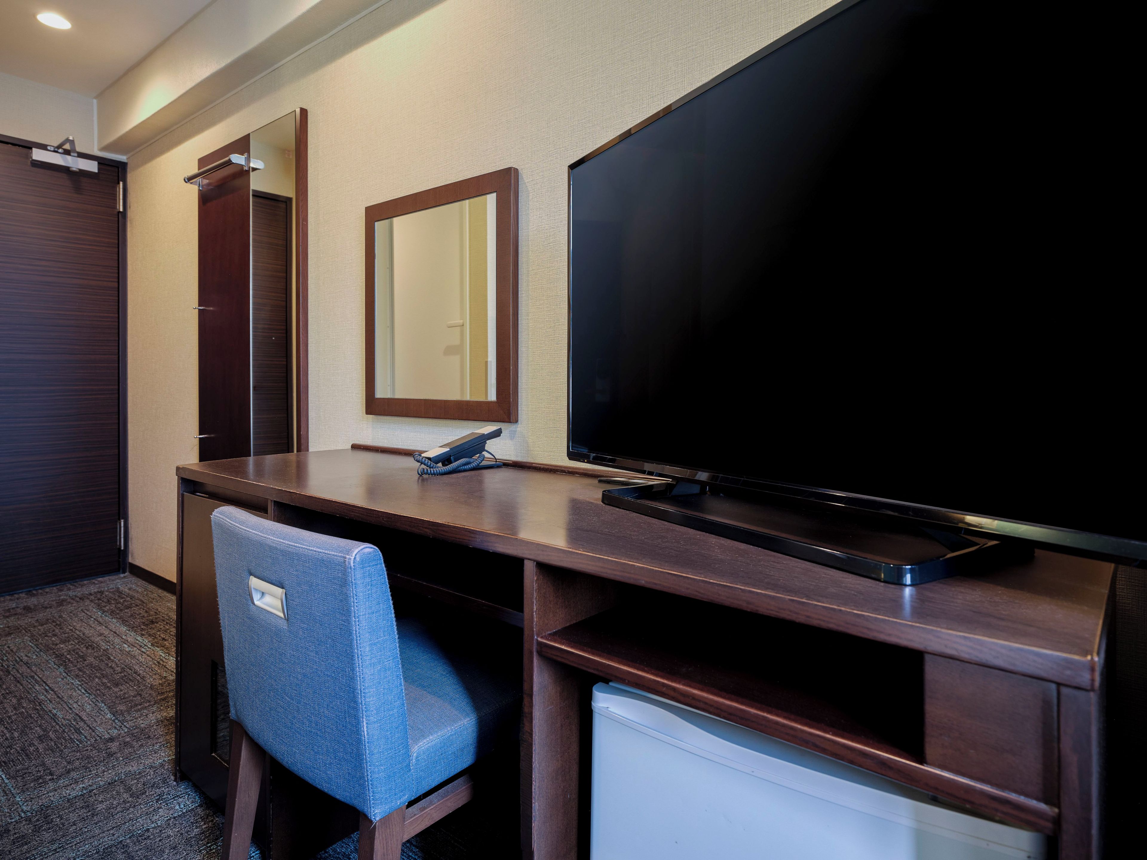 Quarto de hotel com escrivaninha, cadeira, televisão, telefone e espelho.