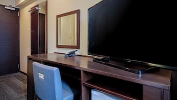 Quarto de hotel com escrivaninha, cadeira, televisão, telefone e espelho.