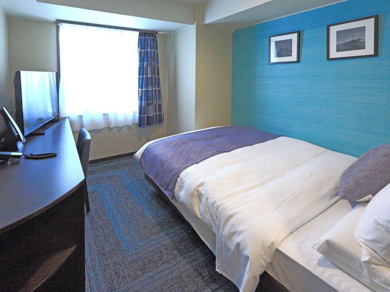 A hotel room with a bed, a desk, a chair, and a window with curtains.