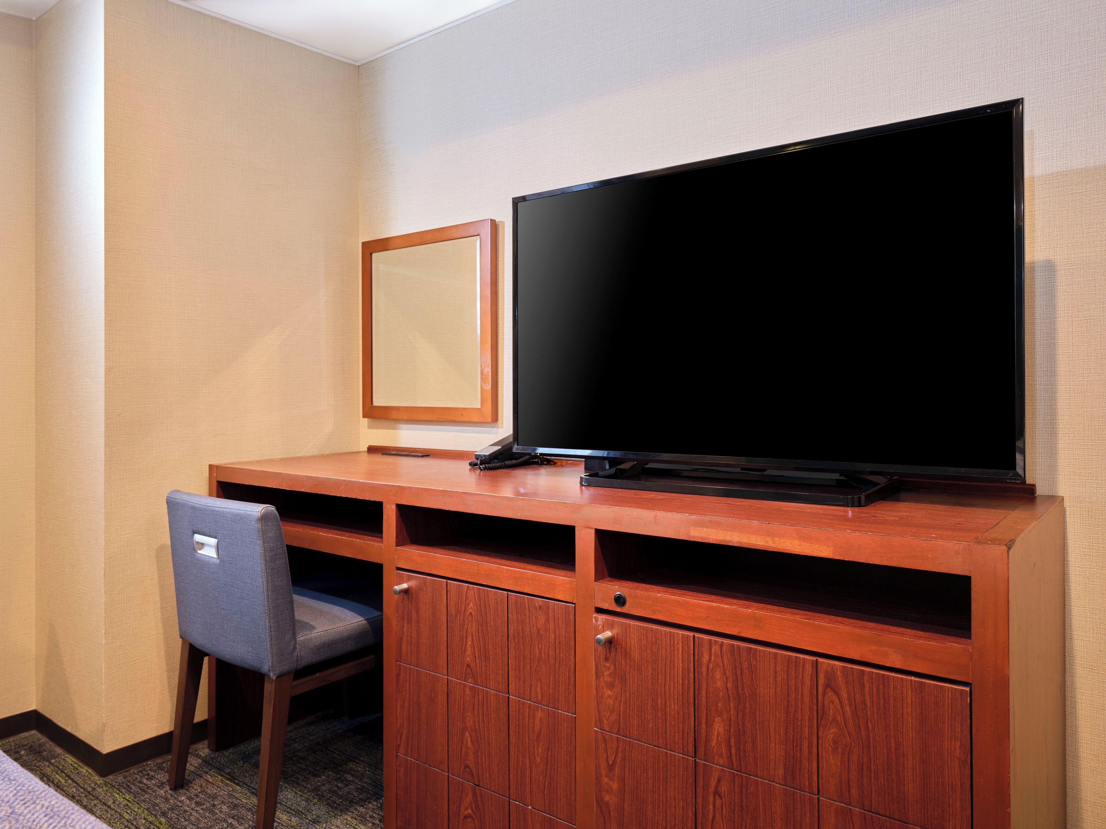 A hotel room with a wooden desk, a television, a chair, and a mirror.