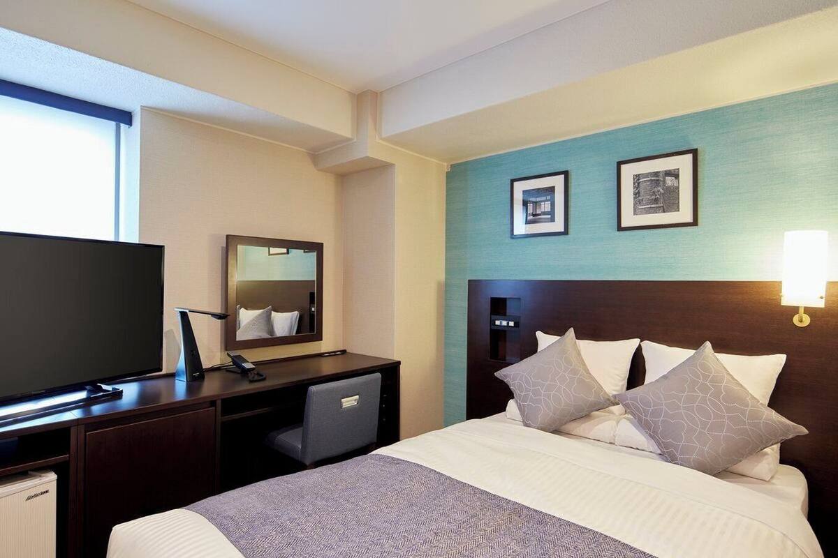 Een hotelkamer met een bed, een bureau met een computer, een televisie en twee ingelijste foto's aan de muur.