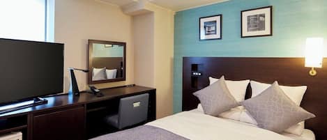 Habitación de hotel con cama, un escritorio con computadora, televisor y dos cuadros en la pared.