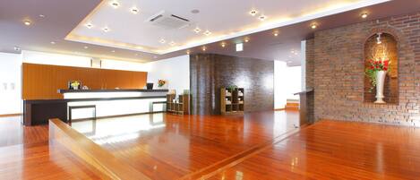 A spacious hotel lobby with a wooden floor, a reception desk, and a brick accent wall.