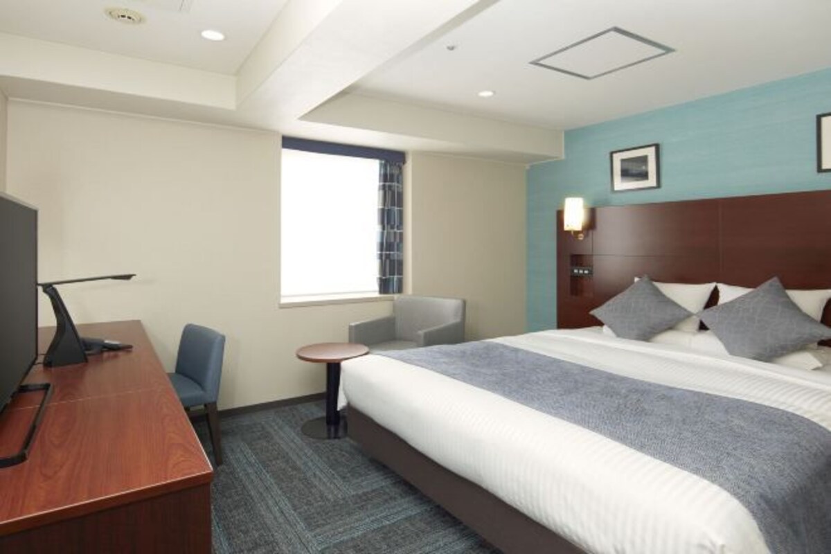 Une chambre d’hôtel avec un grand lit, un bureau, une chaise, une petite table et une fenêtre.