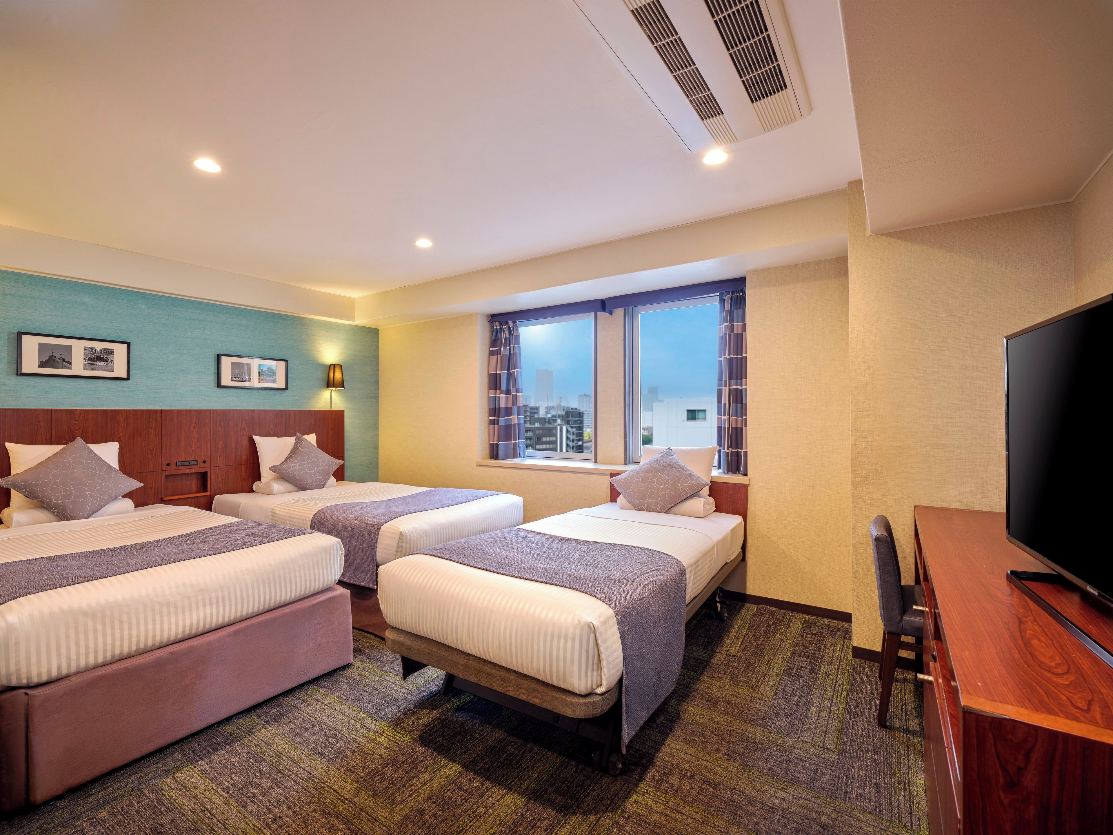 A hotel room with two beds, a television, and a window with a city view.