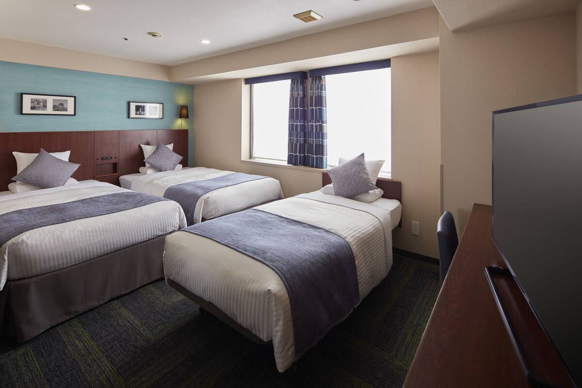 Een hotelkamer met twee bedden, een bureau, een televisie en een raam met gordijnen.
