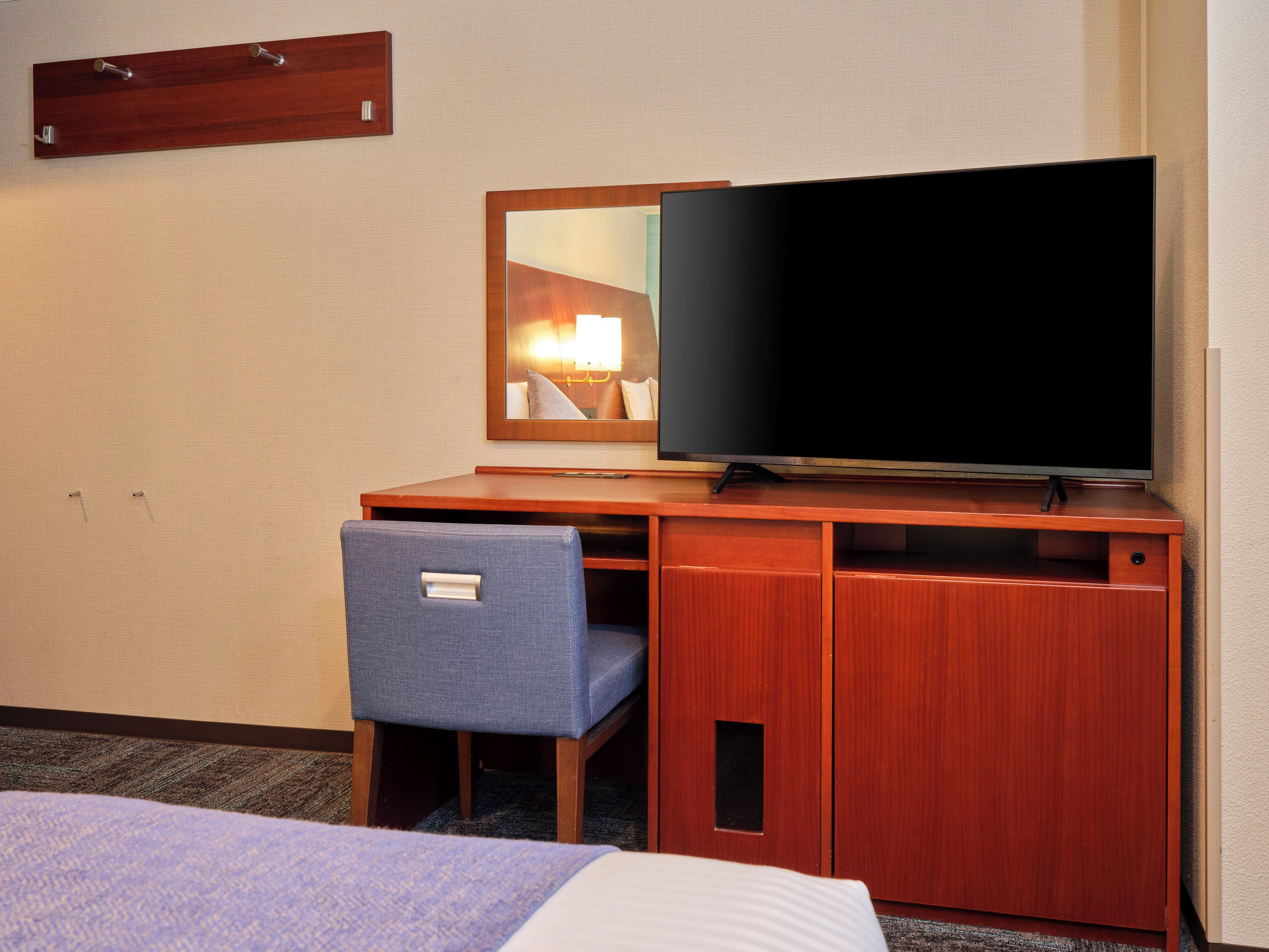 Quarto de hotel com escrivaninha de madeira, televisão, cadeira e cama.