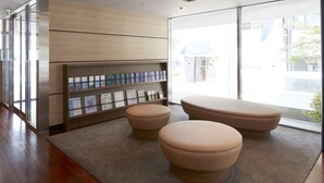 A modern interior with wooden flooring, a beige carpet, and a large window offering a view of the street. - Hotel MyStays Yokohama (Yokohama)