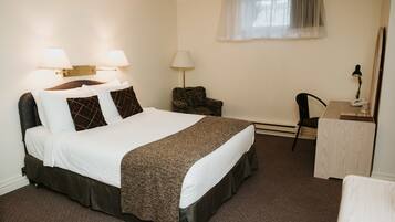A hotel room with a large bed, two bedside lamps, a desk with a chair, and a window with a sheer curtain.
