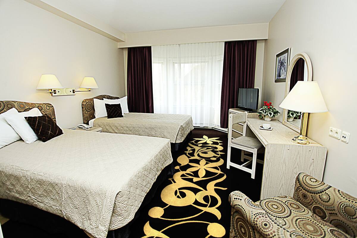 A hotel room with two beds, a desk, a chair, a TV, and a lamp.
