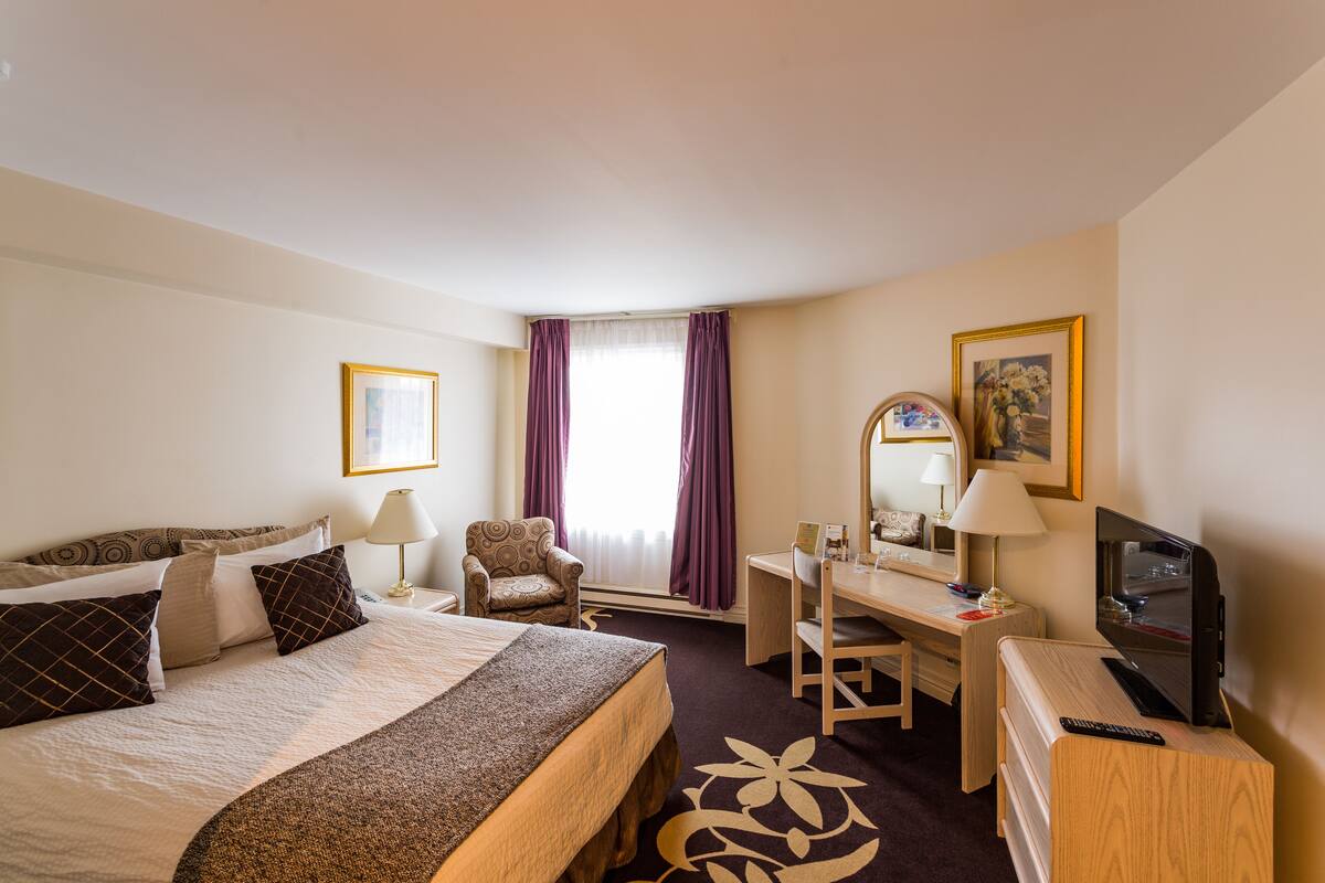 A hotel room with a bed, desk, chair, TV, and a window with curtains.