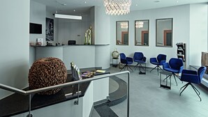 A modern reception area with a curved counter, blue seating, and a unique textured sculpture. - City Hotel (Luxembourg City)