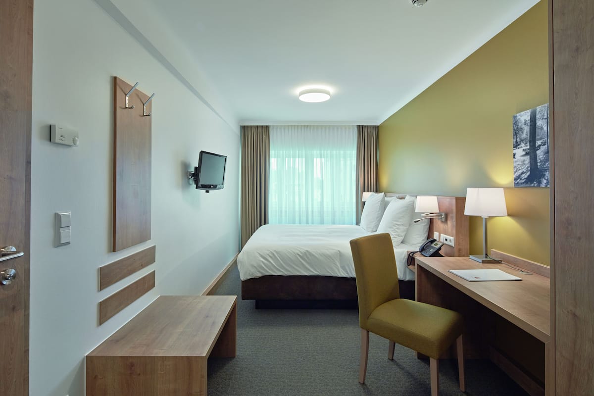 Ein Hotelzimmer mit Bett, Schreibtisch, Stuhl, Fernseher und einem Gemälde an der Wand.