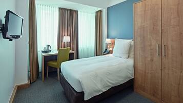 A hotel room with a bed, a desk with a chair, a television, and a wardrobe.