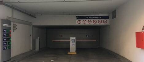 Entrada a un garaje de estacionamiento con un letrero que indica Plaza Liberty, un parquímetro y un extintor.