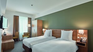 A hotel room with two beds, a desk with a lamp, a chair, and a television. - City Hotel (Luxembourg City)